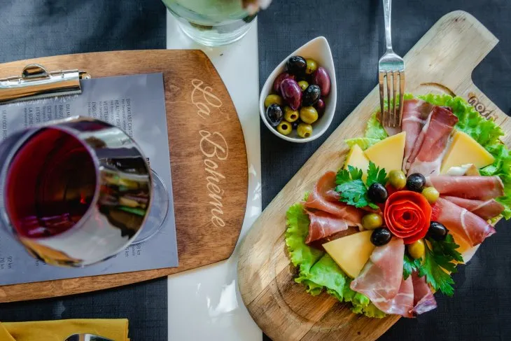  a table with a platter of Dalmatian smoked ham and cheese, a glass of wine on a menu