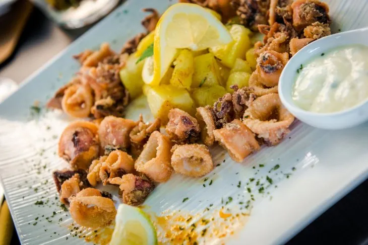  a plate with fried calamari, rosemary potatoes and tartar source 
