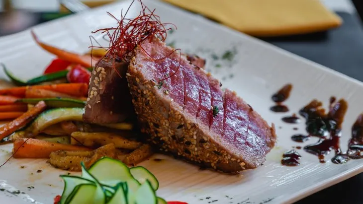  a white plate with tuna steak in sesame and flex seeds with colourful julienne vegetables 