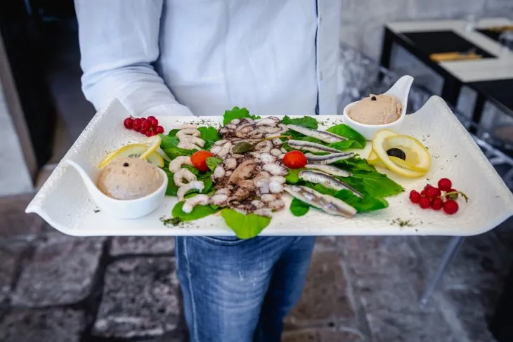 a man holding a plater of octopus carpaccio, fish pate, anchovies and prawns